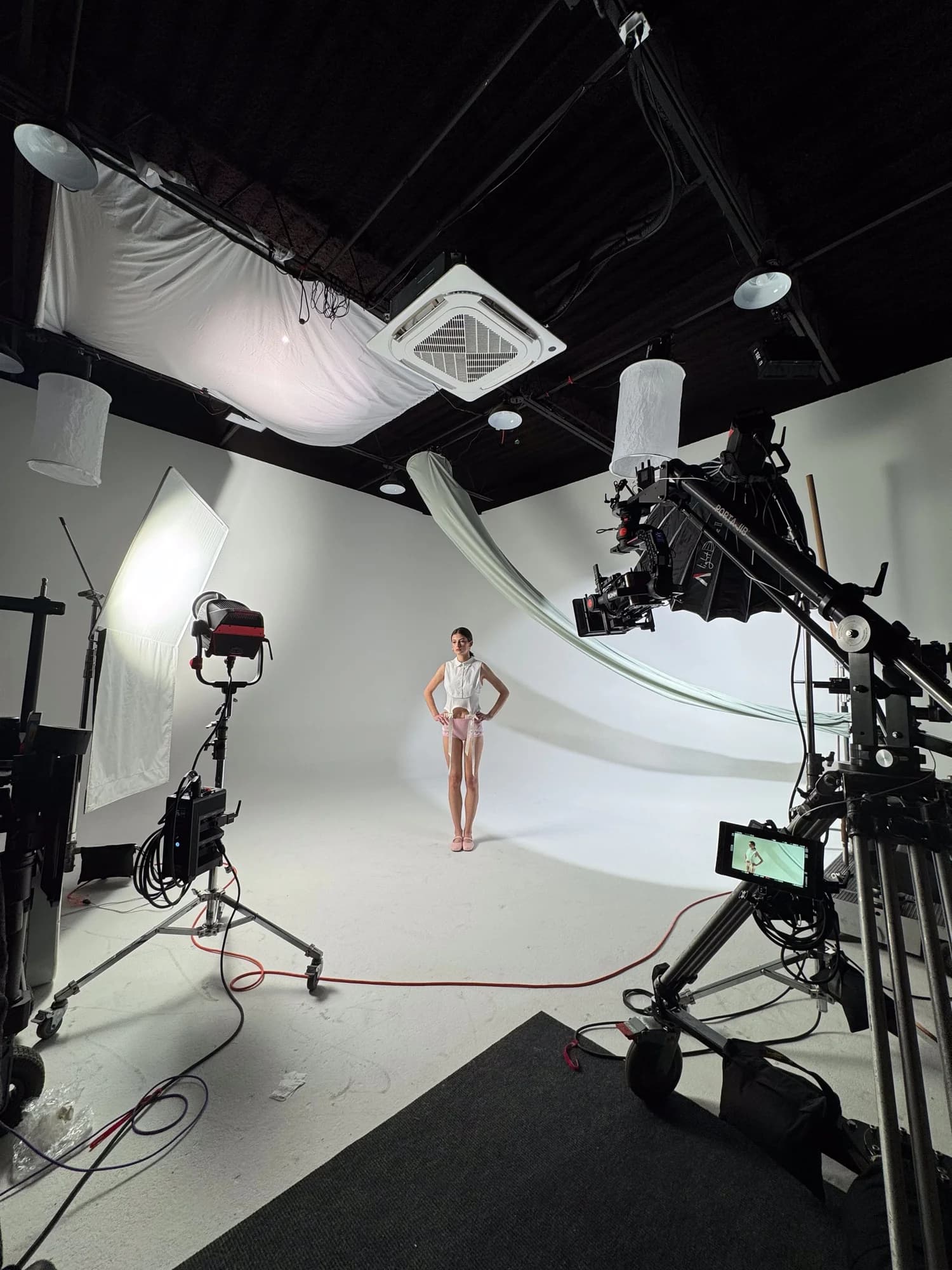 A shoot on the white cyclorama at Studio Bennu: a model in the centre, with lights, a camera on a jib and a monitor around her
